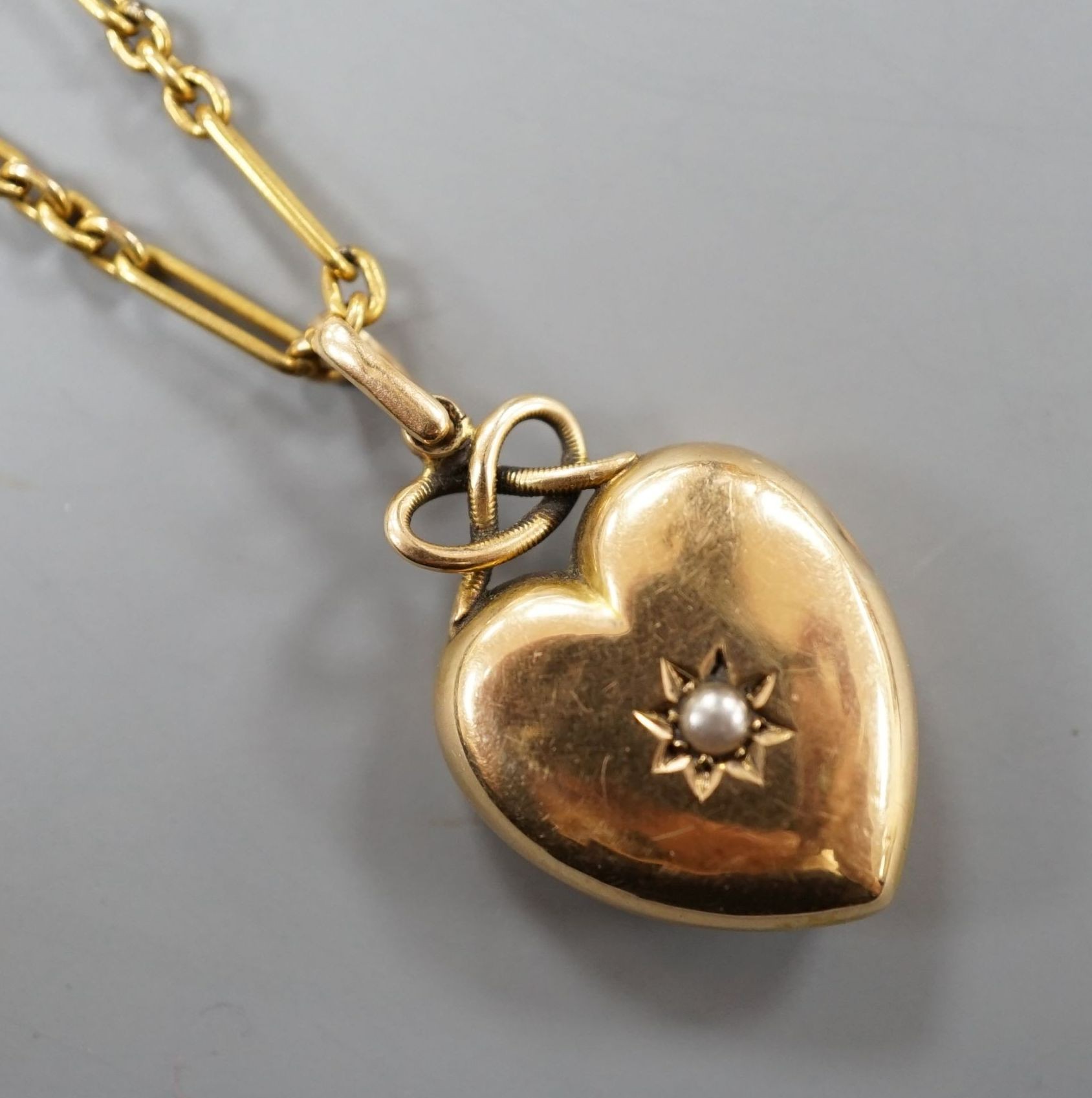 An Edwardian yellow metal and seed pearl set heart shaped locket, with glazed panel back, overall 29mm, on a yellow metal ovoid and spherical link chain, 61cm and a 9c fine link chain (a.f.)
